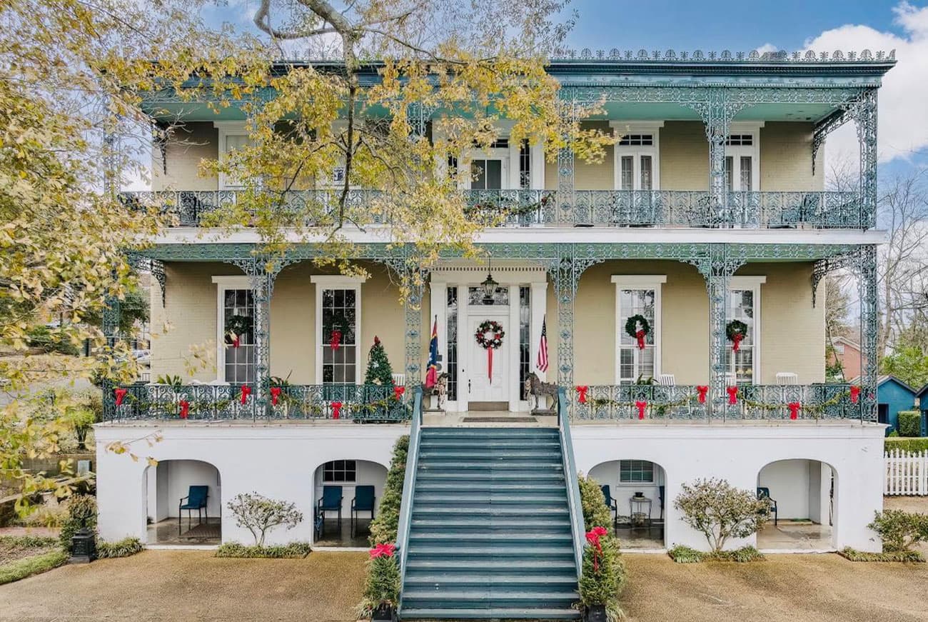 A grand two-story house with intricate ironwork, decorated for the holidays.